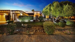 A well-lit courtyard with a paved walkway, neatly trimmed hedges, and a small rock garden. - Bliss: Pool, Spa, Pool Table, Ping Pong, Fire Pit! (Indio)