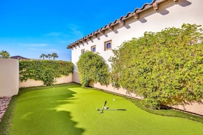 A courtyard with artificial grass, a pool table, and a white building with a tiled roof. - Bliss: Pool, Spa, Pool Table, Ping Pong, Fire Pit! (Indio)
