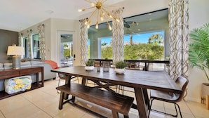 A modern dining area with a wooden table, benches, and a unique ceiling light fixture. - Bliss: Pool, Spa, Pool Table, Ping Pong, Fire Pit! (Indio)
