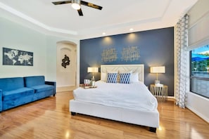 Un dormitorio moderno con una cama grande, un sofá azul, un mapa del mundo en la pared y una ventana con vistas.