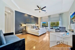A modern bedroom with a bed, bedside tables, a ceiling fan, and a view of the outdoors. - Bliss: Pool, Spa, Pool Table, Ping Pong, Fire Pit! (Indio)