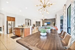 A modern kitchen with a central island, stainless steel appliances, and a dining area with a large wooden table and chairs. - Bliss: Pool, Spa, Pool Table, Ping Pong, Fire Pit! (Indio)
