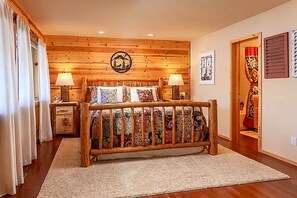 Een houten bed met hoofdeinde, twee nachtkastjes met lampen, een vloerkleed en een muur met een rond embleem.