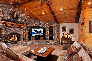 A cozy lodge interior with a stone fireplace, a television, and comfortable seating.