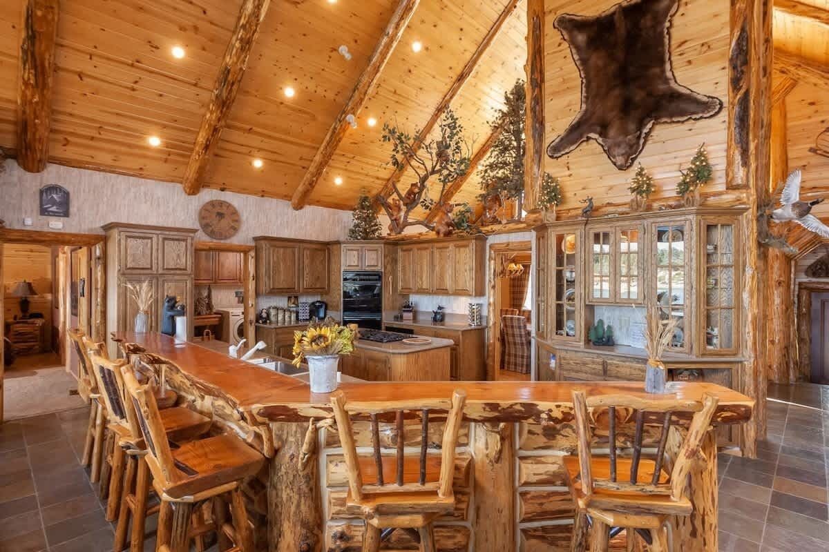 Un interior rústico con una zona de comedor de madera, una cocina con armarios de madera y un techo con un gran cuero de animal.