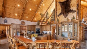 A rustic interior with a wooden dining area, a kitchen with wooden cabinets, and a ceiling with a large animal hide. - Lakefront Luxury Private Dock, Spa & Game Room (Big Bear Lake)