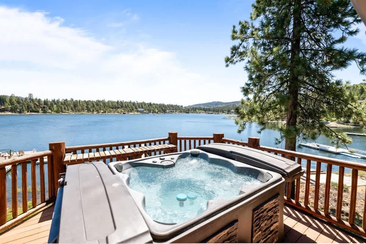 Un jacuzzi en una terraza de madera con vista a un lago y una orilla boscosa.