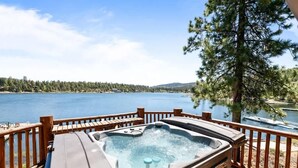 A hot tub on a wooden deck overlooking a lake with a forested shoreline. - Lakefront Luxury Private Dock, Spa & Game Room (Big Bear Lake)