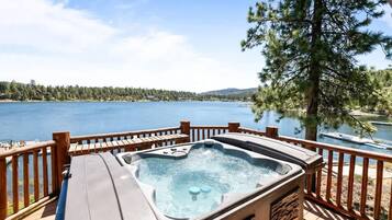 Un jacuzzi en una terraza de madera con vista a un lago y una orilla boscosa.
