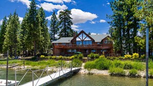 A wooden lodge with a dock extending into a clear lake, surrounded by dense trees. - Lakefront Luxury Private Dock, Spa & Game Room (Big Bear Lake)