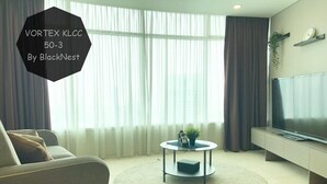 Un salón moderno con un sofá, una mesa redonda de centro, un televisor de pantalla plana y un gran ventanal con cortinas.