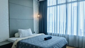 Un dormitorio moderno con una cama grande, una mesita de noche y un ventanal con cortinas translúcidas.