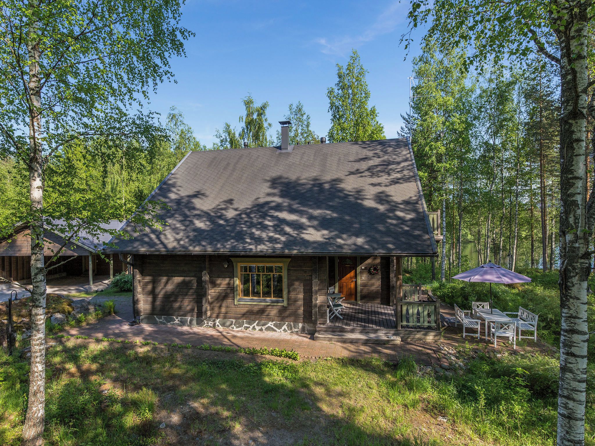 En hytte med veranda, udendørs møbler og udsigt til den omkringliggende skov.