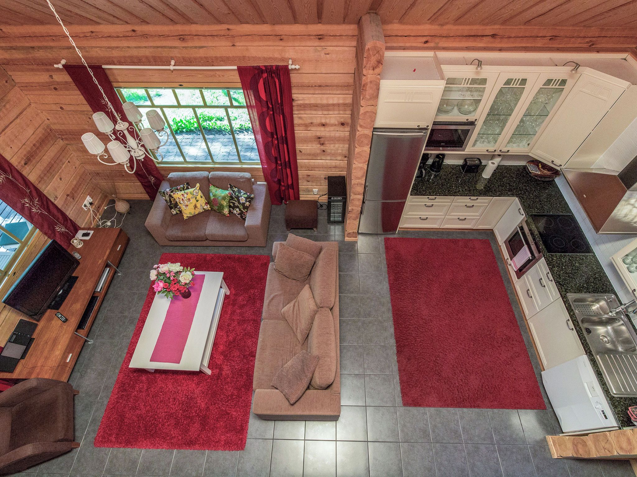 A compact living space with a sofa, a red rug, a small table with a vase, and a kitchenette.