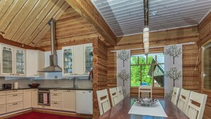 Interior de uma cabana de madeira com cozinha, sala de jantar e grandes janelas.