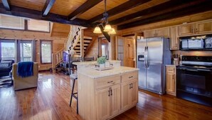 A spacious kitchen with wooden cabinets, a large island, stainless steel appliances, and a staircase leading to an upper level. - MTN VIEWS! True Mtn Wood Cabin-Pool Tble-6x parking-main level master-wifi (Sevierville)