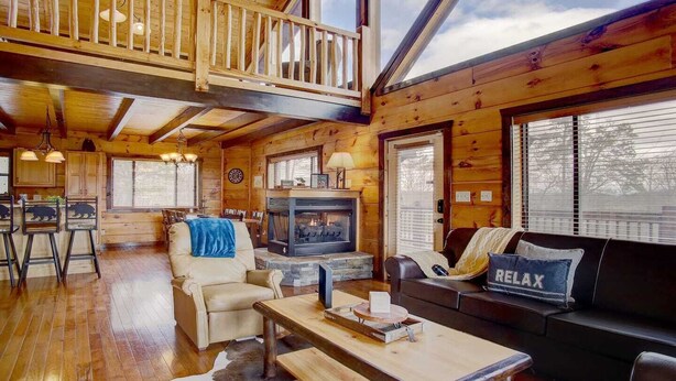 A cozy cabin interior with a fireplace, wooden furniture, and a loft bedroom with a balcony. - MTN VIEWS! True Mtn Wood Cabin-Pool Tble-6x parking-main level master-wifi (Sevierville)