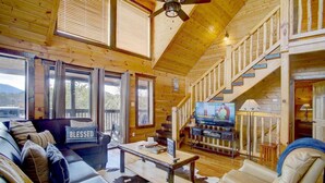 A cozy cabin interior with a wooden interior, a sofa with a 'BLESSED' pillow, a television, and a staircase. - MTN VIEWS! True Mtn Wood Cabin-Pool Tble-6x parking-main level master-wifi (Sevierville)