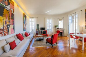 A spacious living room with a sofa, red chairs, a dining table, and a fireplace.