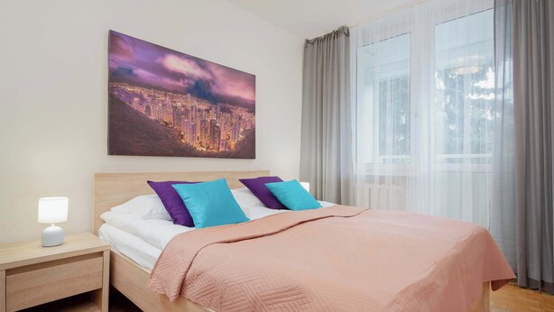 A neatly made bed with a pink blanket, two pillows, and a nightstand with a lamp.