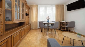 A room with a dining table, chairs, a TV mounted on the wall, and a wooden cabinet with glass doors.