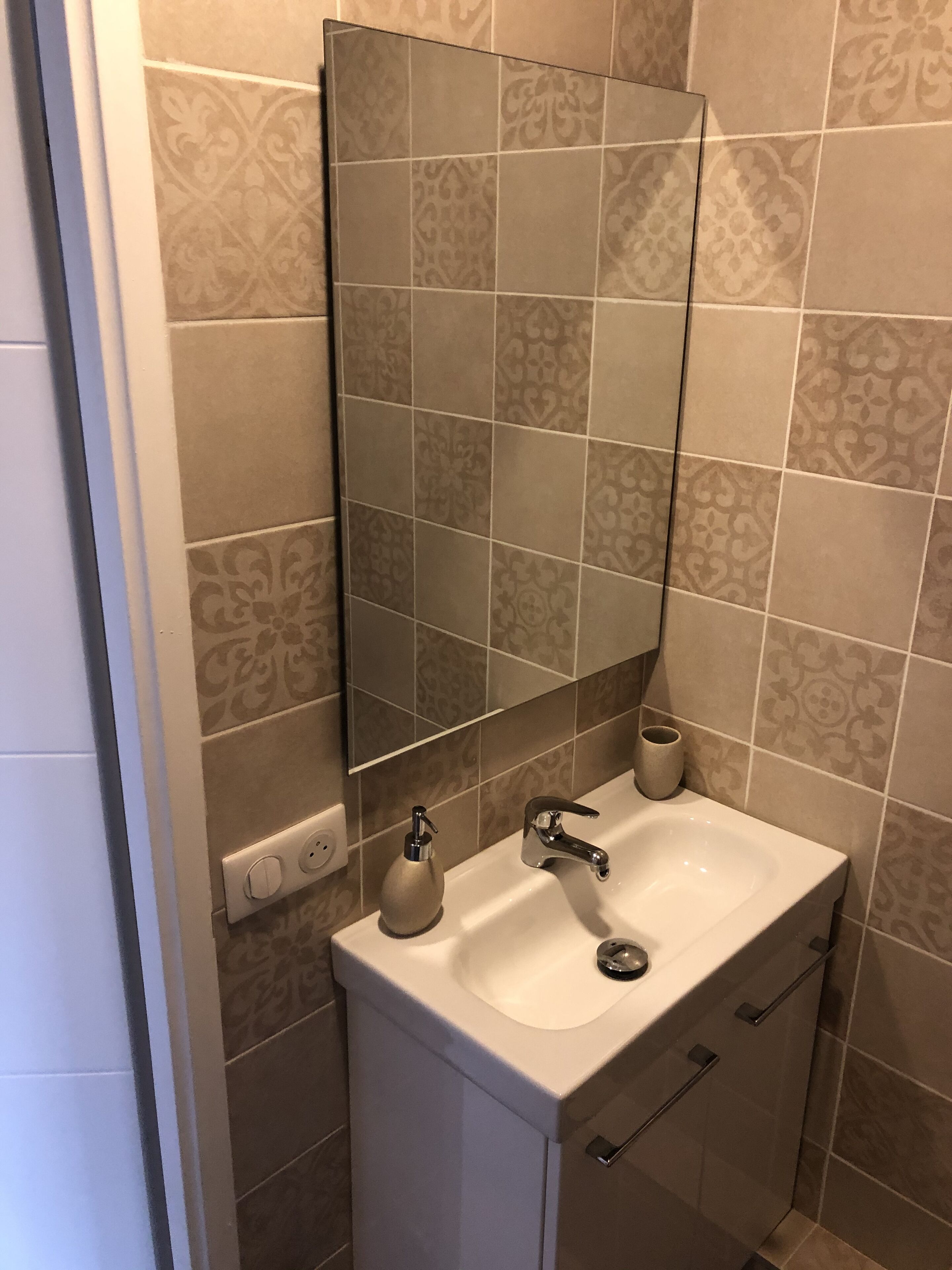 Een badkamer met een witte wastafel, een spiegel en betegelde vloeren.