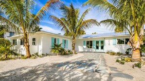 A white building with turquoise shutters, a number '210' on the door, and palm trees in the foreground. - At Last: Ground-level, pool, hot tub, canalfront, dock (Anna Maria)