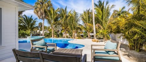 A pool area with lounge chairs and a small table, surrounded by palm trees and a clear blue sky.