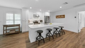 A modern kitchen with white cabinetry, a stainless steel refrigerator, and a central island with bar stools. - At Last: Ground-level, pool, hot tub, canalfront, dock (Anna Maria)