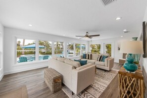 A spacious living room with a large window overlooking a pool area, a ceiling fan, and a modern light fixture.