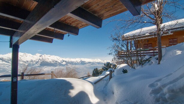 A wooden cabin with a snow-covered roof, a wooden deck, and a view of snow-covered mountains in the background. - Chalet Lisa, ski-in/out, accessible by car (Haute-Nendaz)