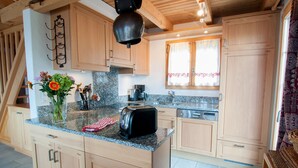 A kitchen with wooden cabinets, granite countertops, a toaster, and a window with curtains. - Chalet Lisa, ski-in/out, accessible by car (Haute-Nendaz)