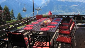 An outdoor dining area with a table set for two, red chairs, and a red umbrella. - Chalet Lisa, ski-in/out, accessible by car (Haute-Nendaz)