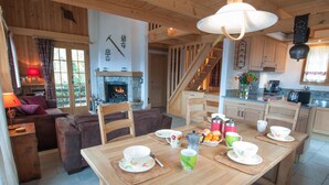A cozy living room with a fireplace, wooden furniture, and a dining area set for a meal. - Chalet Lisa, ski-in/out, accessible by car (Haute-Nendaz)