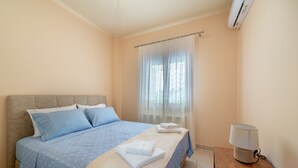 A bedroom with a bed, a bedside table with a lamp, and an air conditioning unit. - Katerina's cozy mountain view apartment (Argostoli)