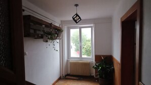 A hallway with a wooden floor, a radiator, a window, and a hanging light fixture. - Large gite with 9 places (Lièpvre)