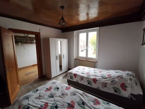 A bedroom with two single beds, a wardrobe, a window with a view of the street, and a ceiling fan. - Large gite with 9 places (Lièpvre)