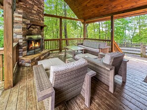 A covered outdoor seating area with a stone fireplace, wicker furniture, and a view of the forest. - Black Dog of Blue Ridge- Pet Friendly | Fenced In Yard | Hot Tub | Outdoor Fireplace (Blue Ridge)