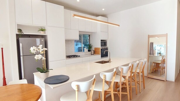 Una cocina moderna con armarios blancos, una isla central con taburetes, un refrigerador de acero inoxidable y un microondas.