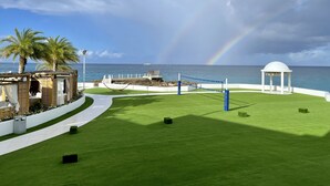 Ein Beachvolleyballfeld am Strand mit einer Laube, Palmen und Blick auf den Ozean.