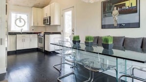 Una cocina moderna con armarios blancos, una mesa de comedor de cristal y un cuadro en la pared.