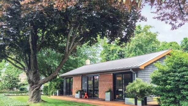 Una casa moderna con techo inclinado, amplias ventanas y una terraza de madera.