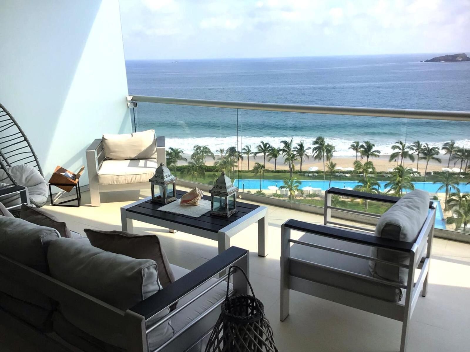 A balcony with a view of the ocean, a pool, and palm trees.