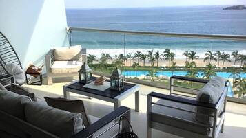 A balcony with a view of the ocean, a pool, and palm trees.
