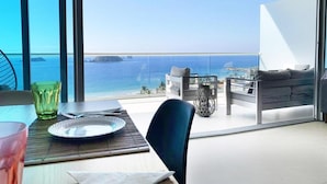 Un balcón con vistas al mar, una mesa de comedor con platos y vasos, y un sofá.