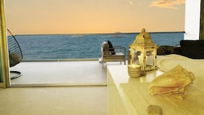 Una habitación con vistas al mar, una mesa blanca con un farolillo y una silla.