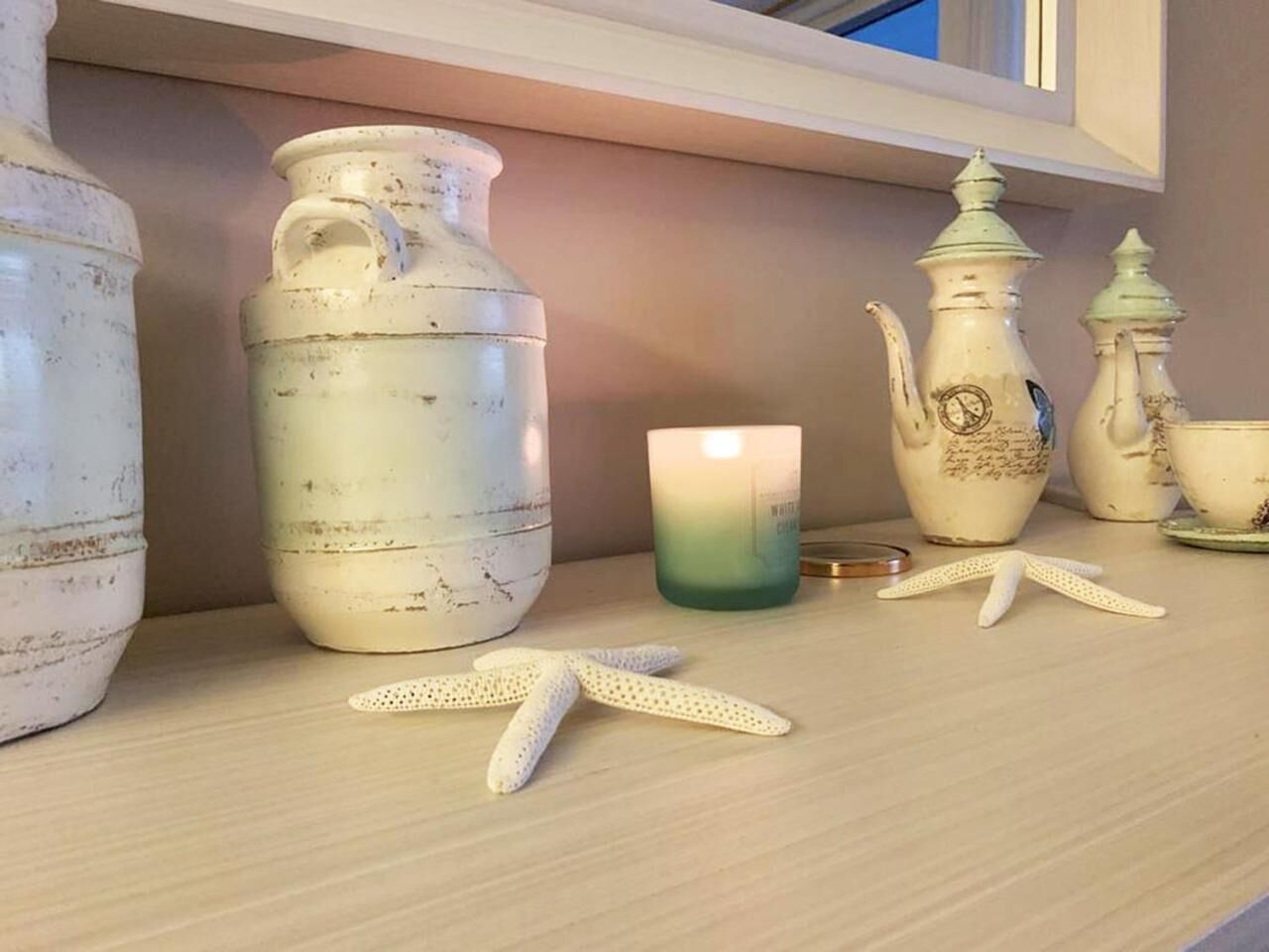 A shelf with various ceramic items including a large jar, a candle, and decorative cups.