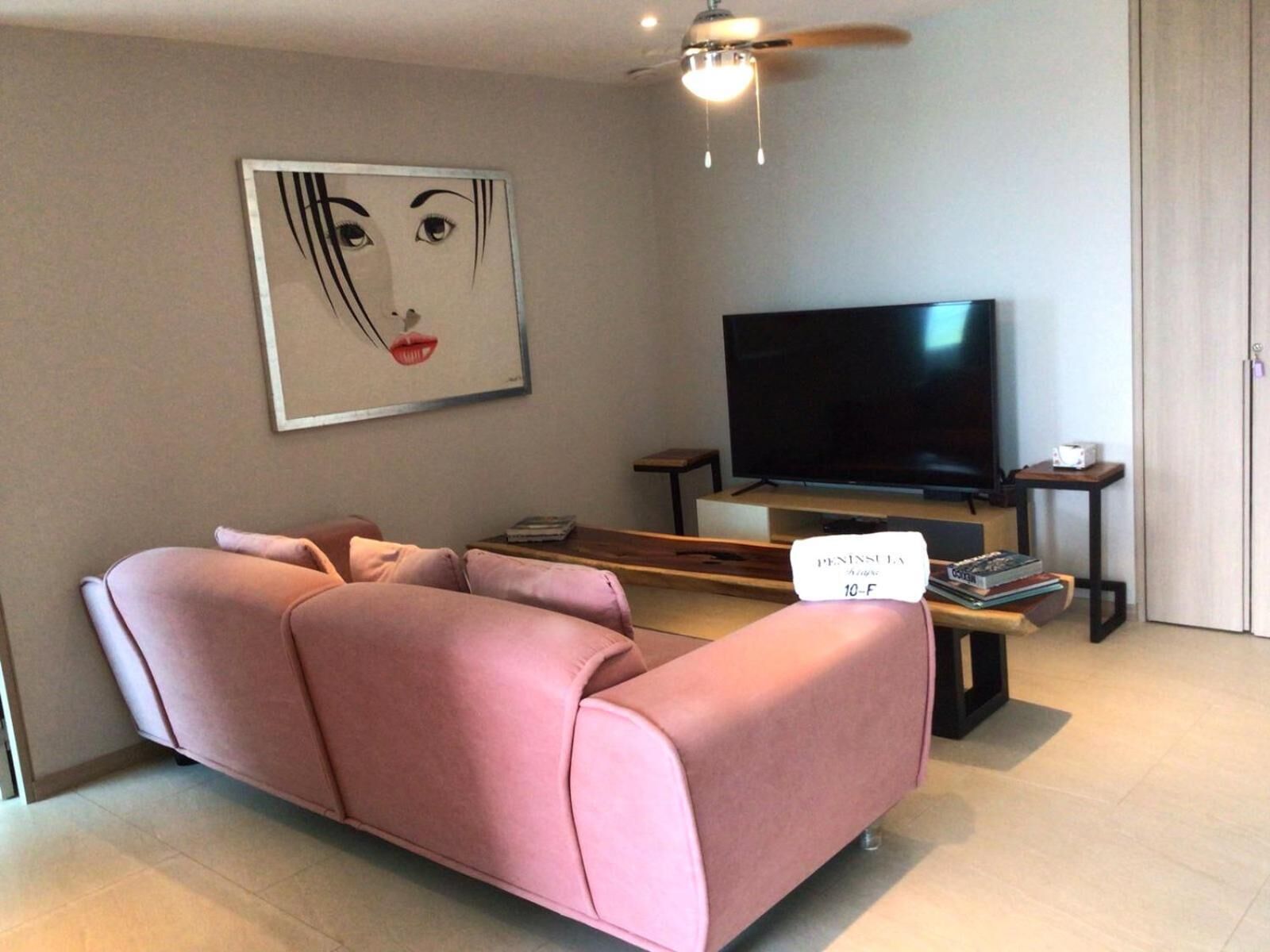 A modern living room with a pink sectional sofa, a flat-screen TV, a ceiling fan, and a bookshelf.