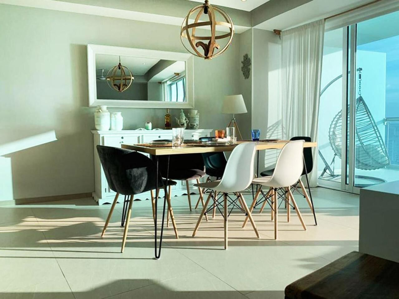 A modern dining area with a round table, black and white chairs, and a hanging light fixture.