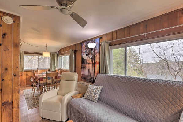 A cozy room with a quilted sofa, a dining table with chairs, and a ceiling fan. - Walk to Marina: Cute Gilford Cottage w/ Grill (Gilford)